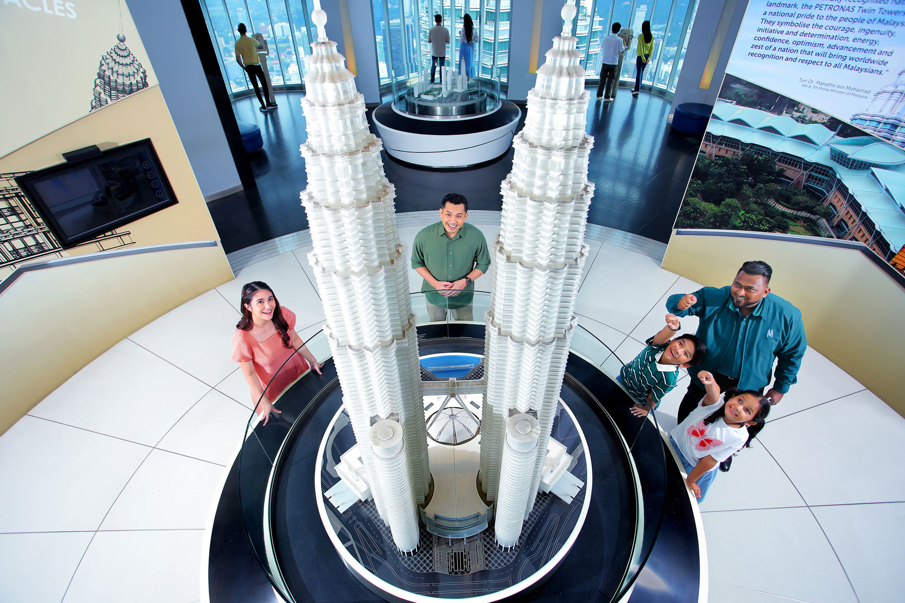 Aerial view of Petronas Towers replica in modern exhibition with adults and children, highlighting education & exploration in a high-tech learning space