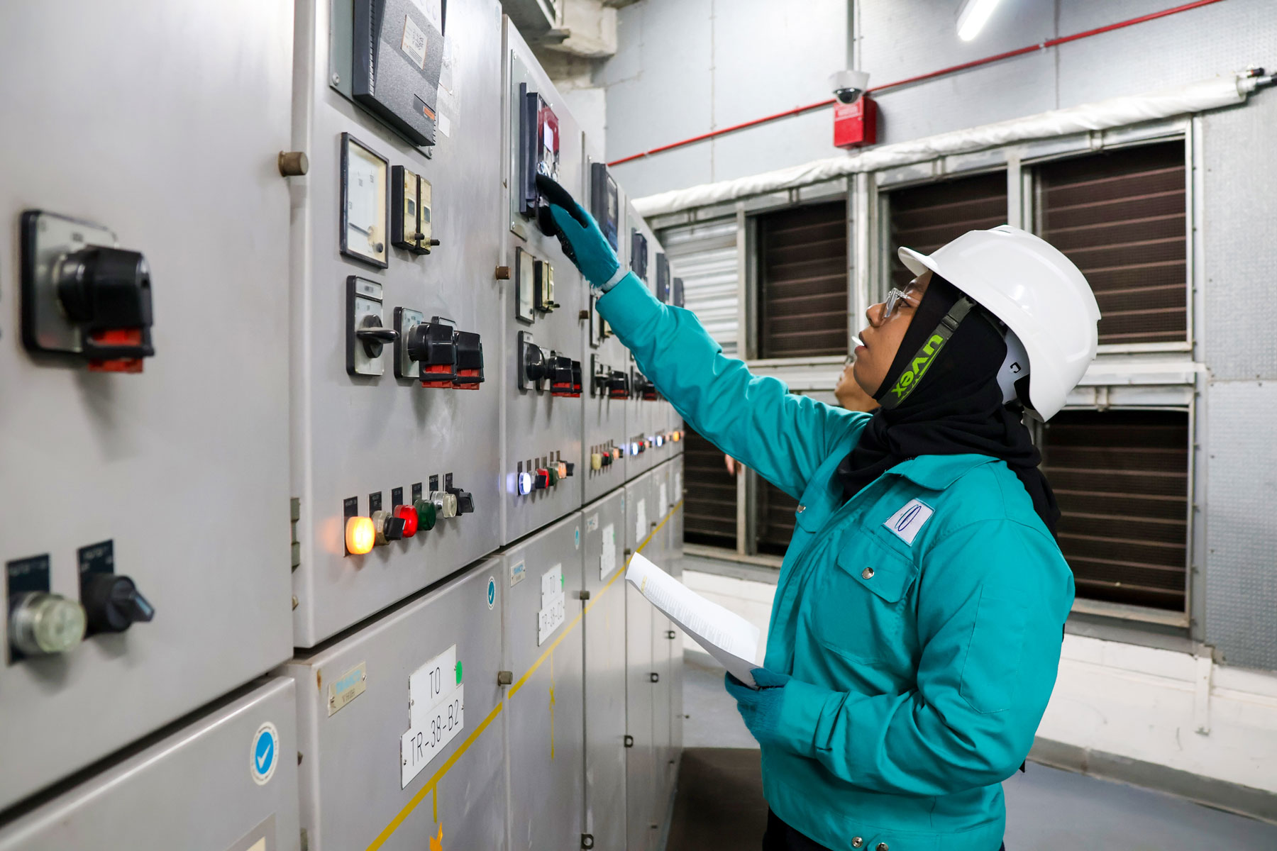 Inspecting electrical panel in industrial control room, demonstrating technical expertise and facility management services